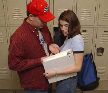 Students in front of lockers using a large binder to shield a drug purchase.
