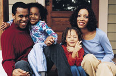 Image of African American family featuring a father, mother, and two young children sitting on a porch.
